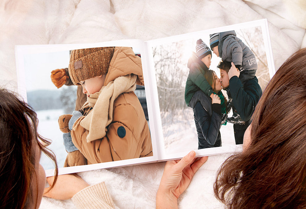 Offenes großes quadratisches Fotobuch mit einem Foto eines warm angezogenen kleinen Jungen auf der linken Seite und einer Familie mit einem sich küssenden Paar auf der rechten Seite.