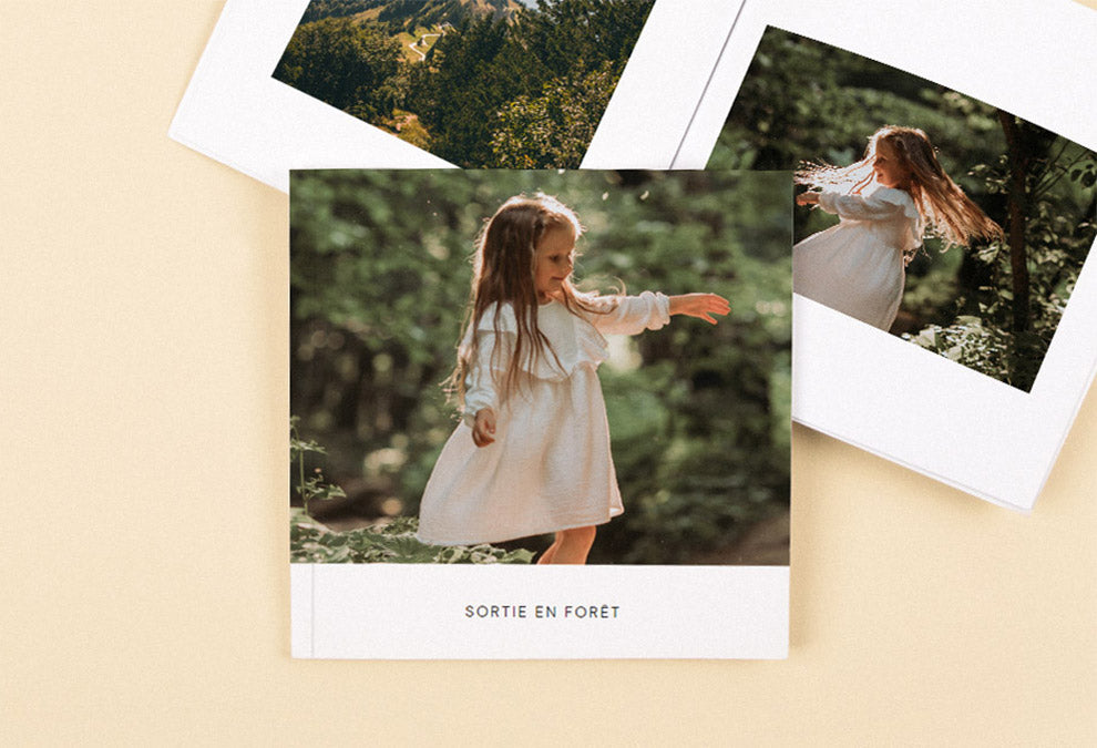 Deux livres photos moyens carrés dont l'un est ouvert sur avec une photo de forêt à gauche et une petite fille dans la nature à droite et l'autre fermé avec une photo d'une petite fille dans la nature et le texte "sortie en forêt" sur la page couverture.