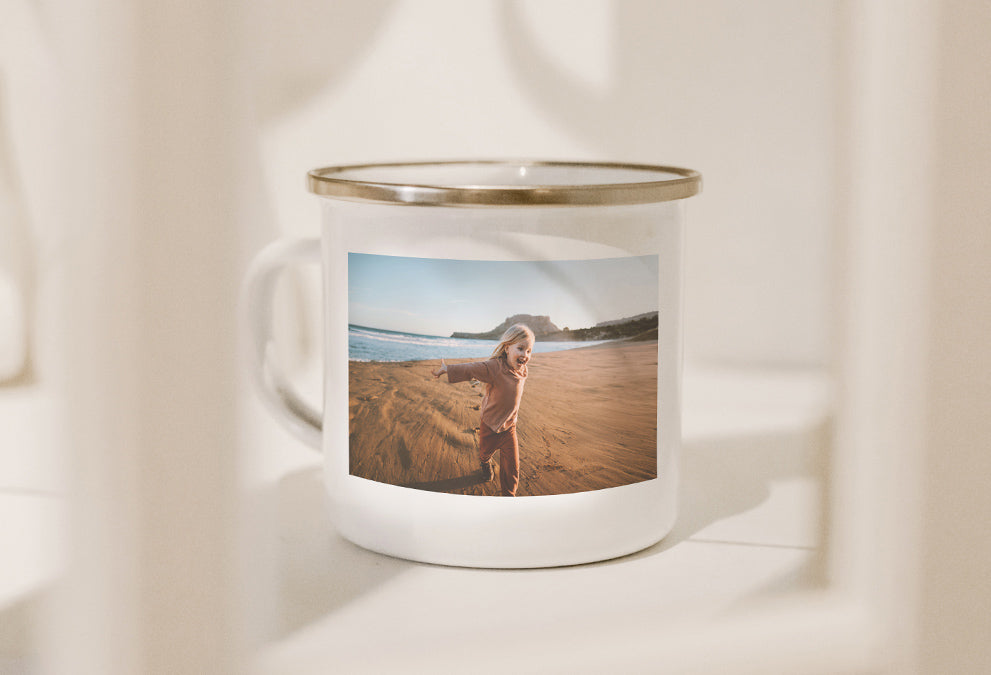 Personalisierte weiße Emaille-Tasse mit Goldrand und einem Foto eines Kindes, das am Strand läuft.