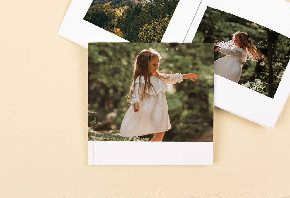 Zwei mittelgroße quadratische Fotobücher, von denen eines offen auf mit einem Waldfoto links und einem kleinen Mädchen in der Natur rechts und das andere geschlossen mit einem Foto eines kleinen Mädchens in der Natur und dem Text „Ausflug in den Wald“ auf der Titelseite ist.