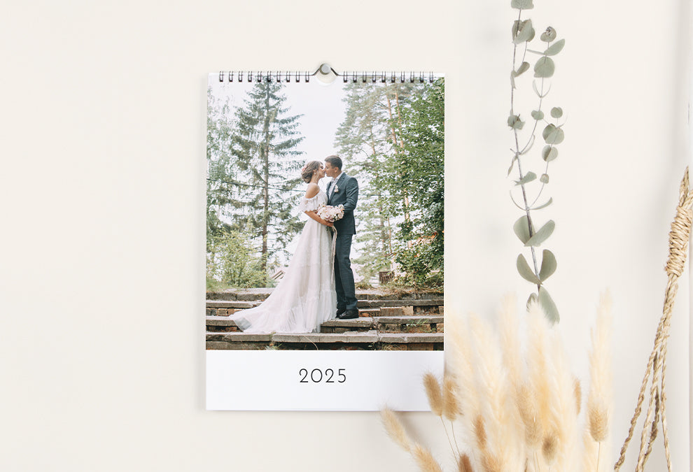 Calendrier murale A4 portrait accroché à un mur et ouvert sur la page de couverture qui montre avec une grande photo de mariage et l'année 2025 en bas.